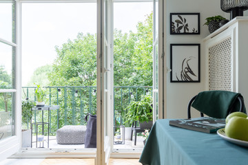 Open balcony door with a view of trees. Pouf and table on a balcony. Real photo