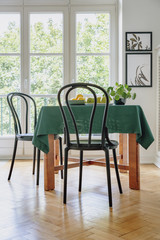 Black chair next to a table with green cloth in a dining room interior. Balcony window in the background. Real photo
