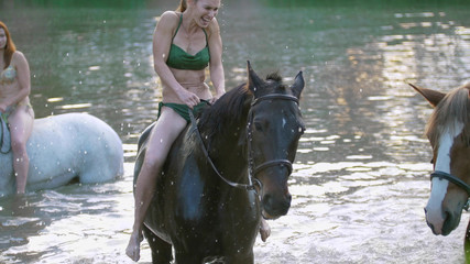Bikini dressed girls walking on horses in river