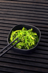 Salad from green algae in a black bowl on a black background.