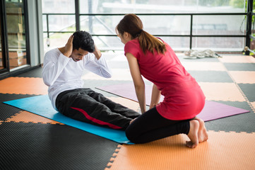 sportsman sit ups in gym with assistance of female friend in gym.