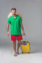 traveler with mexican sombrero walking with yellow baggage on grey