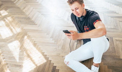 Young man using his smartphone with headphones, listen the music and sit on the floor