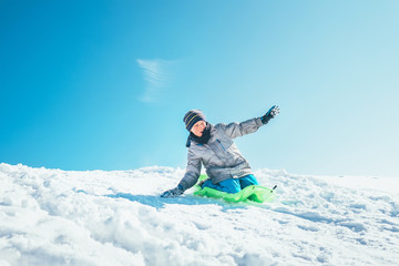 Naklejka na ściany i meble Boy slides down from the snow slope. Enjoying the winter sledding time