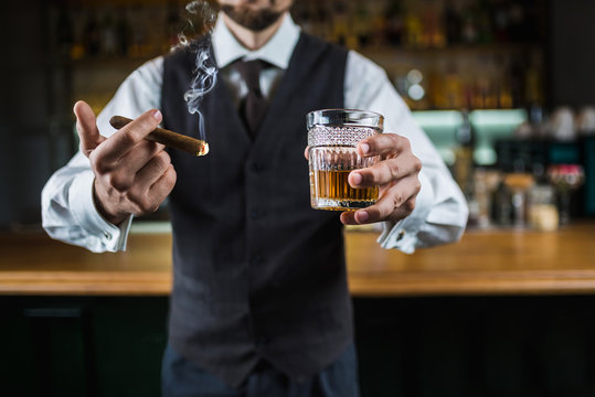 elegant businessman is smoking cigar and holds whiskey glass on the bar counter. No face