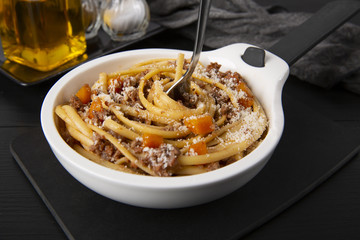 Pasta with Bolognese sauce. Parmesan and olive oil. Spaghetti is screwed onto the fork. In a white frying pan. The background is black. Italian food.