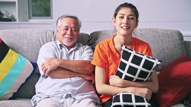 Old man watching TV with his daughter in living room in early evening. Enjoying entertainment together, senior asian man and young woman. Senior lifestyle family concept.Scare look.