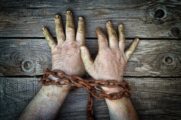 Dirty male hands chained with old rusty thick chain on the wooden boards with a vignette