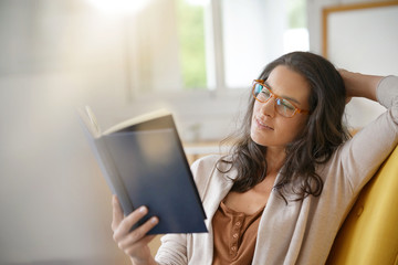 Brunette woman at home reading book - Powered by Adobe