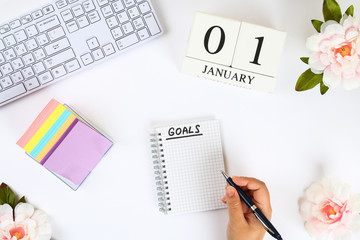 Write a goal for the new year 2010 in a white notebook on a white desktop next to a coffee mug and a keyboard. Top view, flat layout.