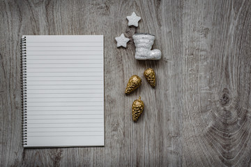 Christmas decorations, Santa's white boot, golden fir cones, snowflakes and an open blank notebook, wooden background