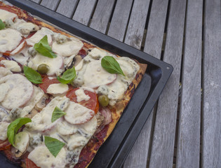 Home made Close up from above on italian freshly home made organic pizza with tomatoes, cheese, onion, olives and green basil leaves on baking tray on vintage wood table background