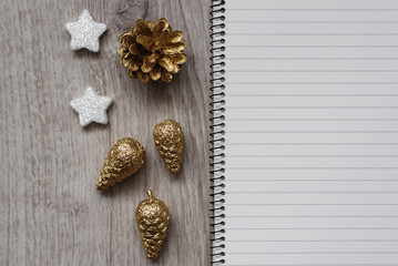Christmas decorations, Santa's white boot, golden fir cones, snowflakes and an open blank notebook, wooden background