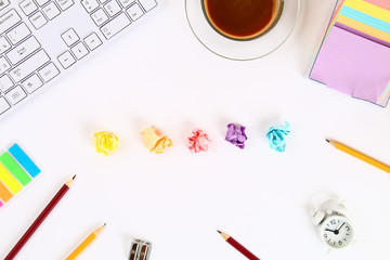 Crumpled multicolored sheets of paper on a white desktop next to a coffee mug and a keyboard. Top view, flat layout. Copy the space.