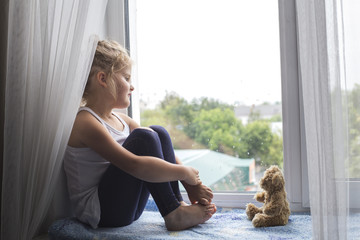Girl sitting on the window sill and looks out the window