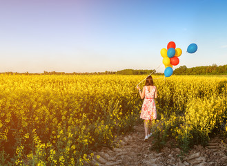 walking girl with bunch of balloons in blooming field