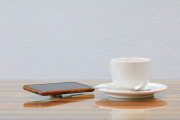 coffee cup white and mobile phone on the glass table wooden and a cement wall background. copy space