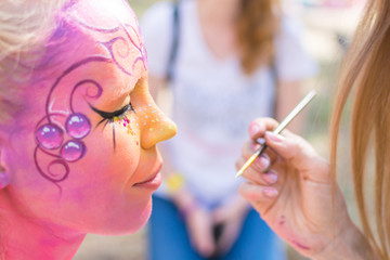 A woman's face painted in a fairy-tale character. Applying a pink aqua-color to the face.