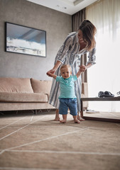 Mother helps and supports the child learning to walk. The child enjoys the first steps. © luckybusiness