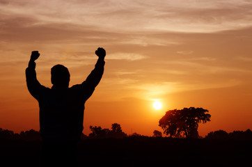 Silhouette of a man with hands raised and sunrise sky background