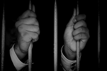 Close-up Of Businessman Hand Holding Metal Bars In Jail with dark environments.