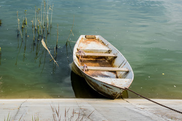 Obraz premium Old wooden boat greenish muddy river. Next to the old wooden oar. Local and rural landscape. Simple and rustic but with rusty grades, parked near a rusty concrete shore.