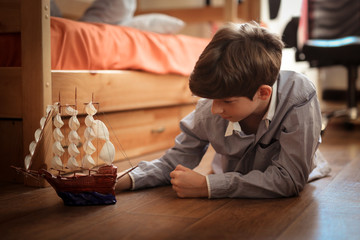 Fototapeta na wymiar teen plays with ship model on floor in real room