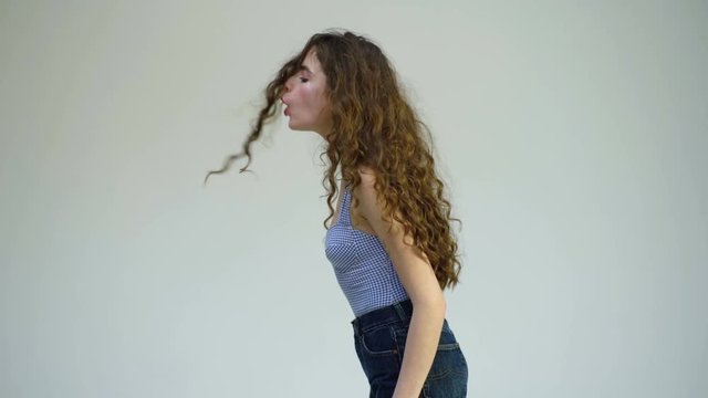 A curly girl blowing on her hair on a white background. Fashion look and beauty concept. Parisian fashion and style of pretty woman with long curly hair.