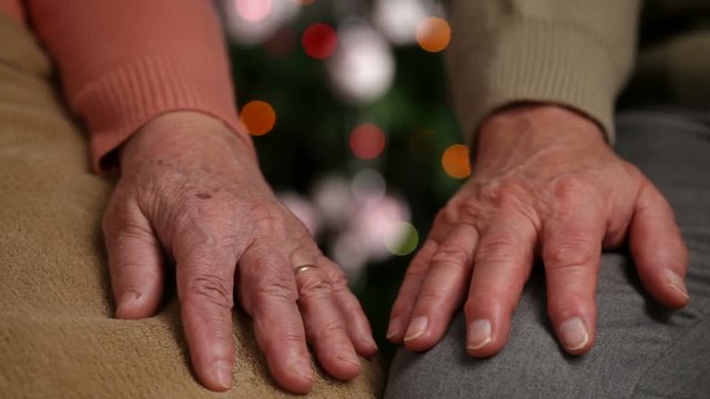 Senior hands of woman and man resting in front of christmas tree waiting - old age concept, closeup, shallow depth, camera dolly