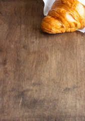 Fresh croissant into the paper on old wooden background