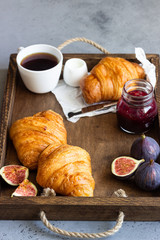 Old wooden tray with cup of coffee, jam in jar, fresh figs and croissants. Breakfast time