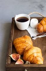 Old wooden tray with cup of coffee, jam in jar, fresh figs and croissants. Breakfast time
