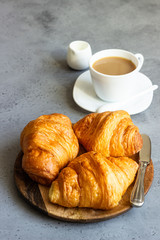 Fresh butter croissants on wooden plate on grey concrete background.