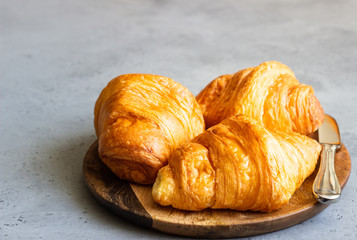 Fresh butter croissants on wooden plate on grey concrete background.