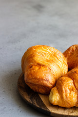 Fresh butter croissants on wooden plate on grey concrete background.