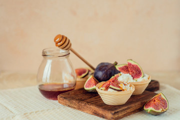 Autumn dessert: tartlets baskets with ripe figs, soft cheese and honey on a light background.