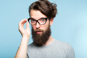 eccentric teacher or quirky it guy. bearded hipster dude wearing cat eye glasses. stylish modern fashionist. portrait of a geeky foppish man on blue background.