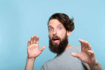 surprised startled shocked man. gasping of fright. portrait of a taken aback bearded guy on blue background. emotion facial expression. people reaction concept.