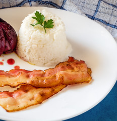 Pile of white rice, onion and bacon on a white plate on blue table, towel texture