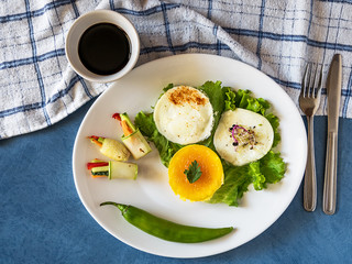 Fried eggs on a green leaf with rolled salad on white plate, with sauce, view from above, towel texture, knife and fork