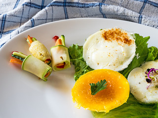 Fried eggs on a green leaf with rolled salad on white plate, view from above, towel texture