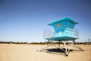 A deserted blue lifeguard station on a beach with buildings and trees in the background in a summer beach landscape
