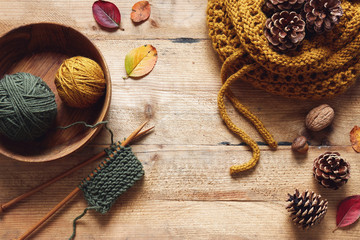 A piece of knitting with wooden needles and yarn among leaves and pine cones.