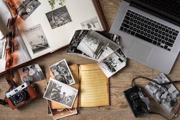 Old family photos on wooden background. Vintage pictures, camera, notepad and modern notebook. Flat...