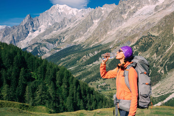 Fototapeta na wymiar woman hikerdrinks water, standing on a mountain background, Mont Blanc massif. Travel around Mont Blanc with a backpack.