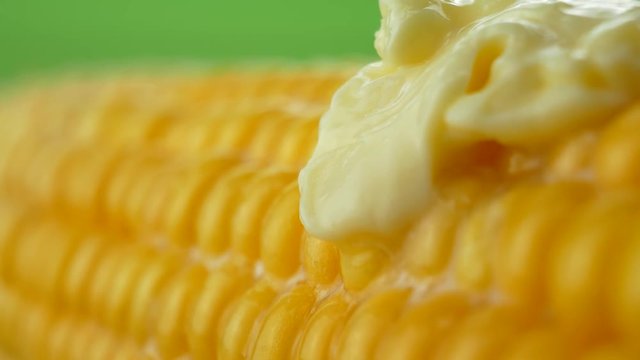 Fresh piece of hot butter melting on ripe yellow fresh corn on cobs at green background