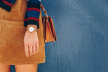 close up, young fashion blogger wearing a corduroy dress and a white and golden analog wrist watch. checking the time, holding a beautiful  leather purse. street style fashion details.  - obrazy, fototapety, plakaty