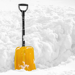 Yellow plastic shovel stuck upright in fluffy pile of white snow in winter. Picture with copy space...