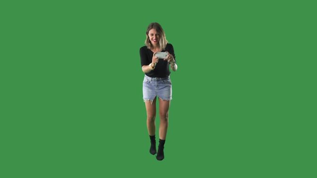Young woman photographing with smart phone camera. Full body isolated on green screen background. 
