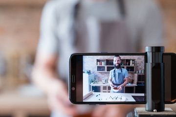 food blogger streaming live. bearded hipster man communicating with subscribers through phone camera. chef cooking pie.